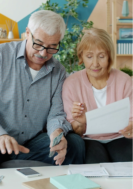 An older couple on a sofa reviewing household bills and paperwork together